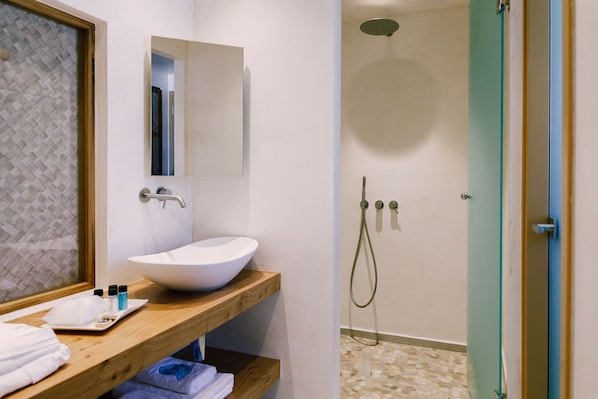 A bathroom with a wooden vanity, a white sink, and a shower area with a glass door. - Opalia Suites (Santorini)