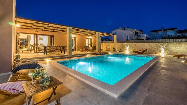 A swimming pool with a tiled deck, outdoor seating, and a covered area with a table and chairs. - Villa Skyfall (Bibinje)