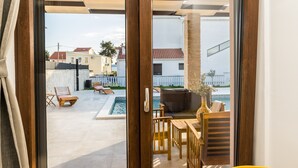 A view through a glass door into a pool area with lounge chairs and a table. - Villa Skyfall (Bibinje)