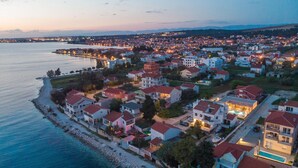 An aerial view of a coastal town with houses along the waterfront, a promenade, and a bridge connecting the town to the mainland. - Villa Skyfall (Bibinje)