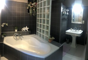 A modern bathroom with a freestanding bathtub, a pedestal sink, and dark tiled walls.