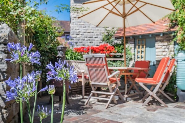 A patio with outdoor furniture, a stone wall, and flowering plants.
