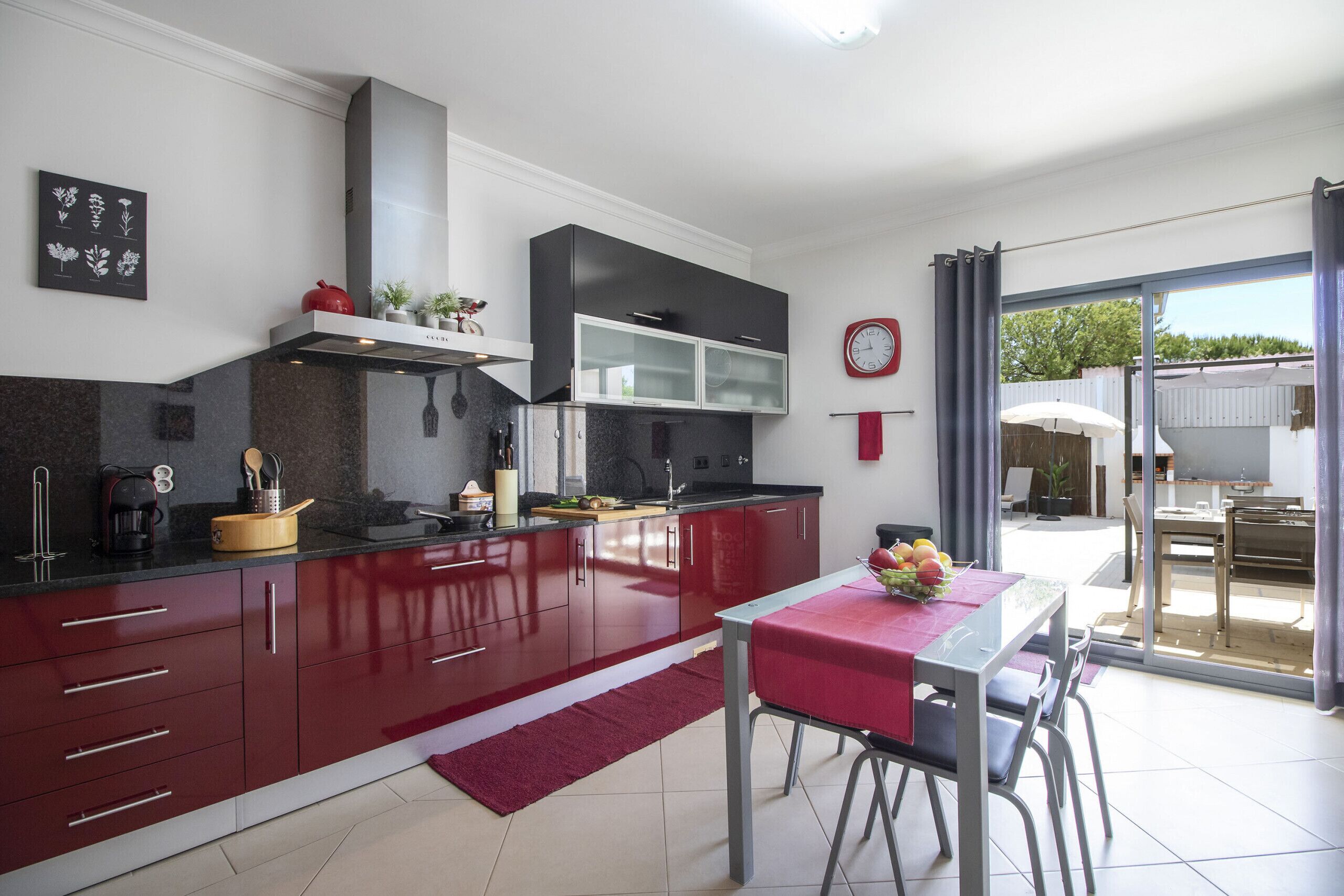 Una cocina moderna con armarios rojos, una encimera negra y un comedor con mantel rojo.