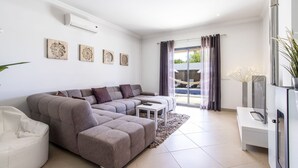 A modern living room with a sectional sofa, a small white coffee table, and a large window with curtains. - Villa Maya | 3 Bedrooms | Modern | Almancil (Almancil)