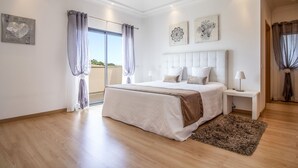A bedroom with a large bed, a bedside table with a lamp, a view of the outdoors through a sliding door, and two wall art pieces. - Villa Maya | 3 Bedrooms | Modern | Almancil (Almancil)