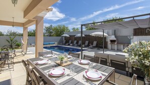 An outdoor patio with a pool, dining tables set for four, and lounge chairs. - Villa Maya | 3 Bedrooms | Modern | Almancil (Almancil)