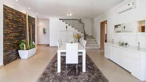 A modern kitchen with white cabinets, a dining area with a white table and chairs, and a staircase leading to another level. - Villa Maya | 3 Bedrooms | Modern | Almancil (Almancil)