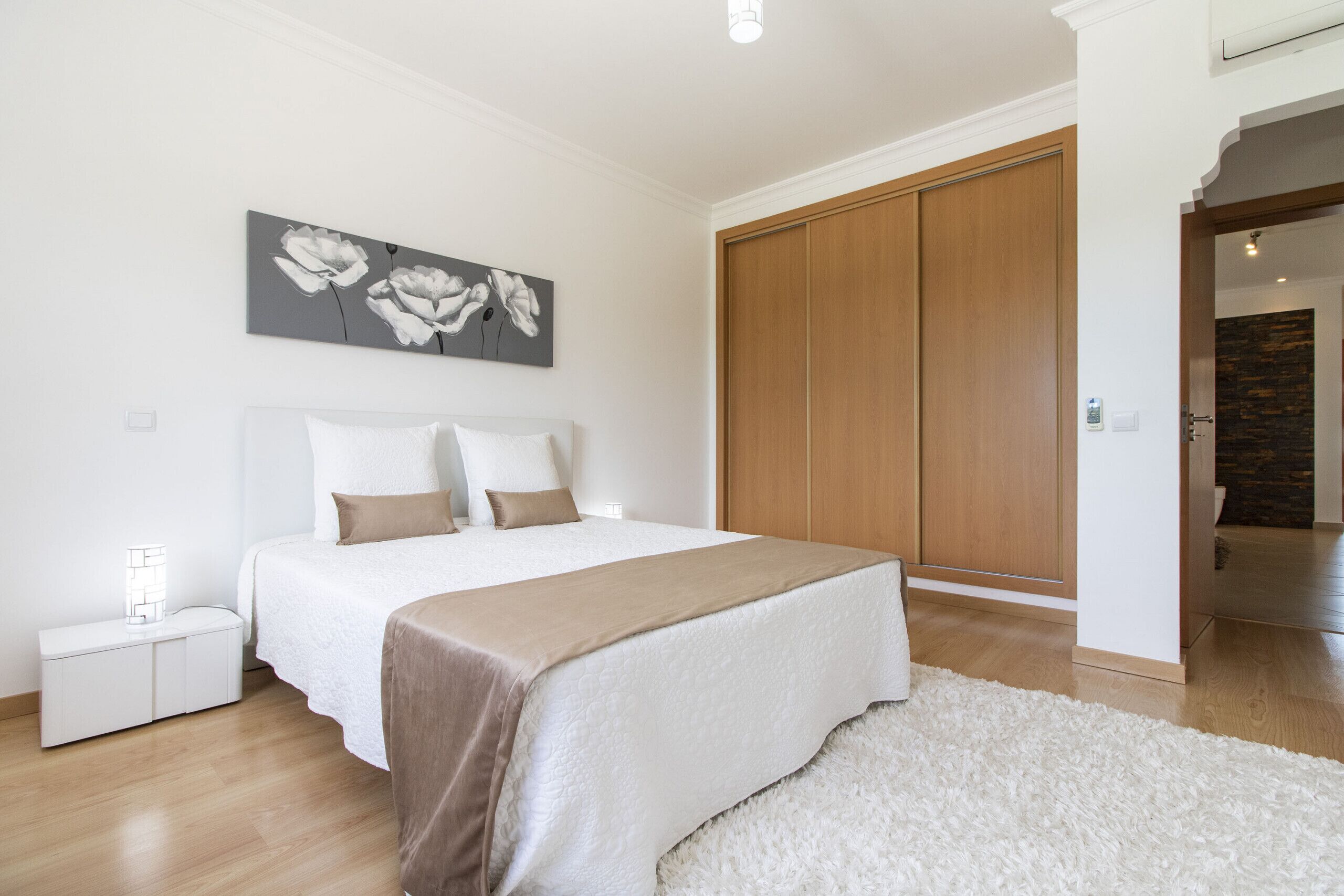 A bedroom with a bed, a nightstand, a wardrobe, and a painting on the wall.
