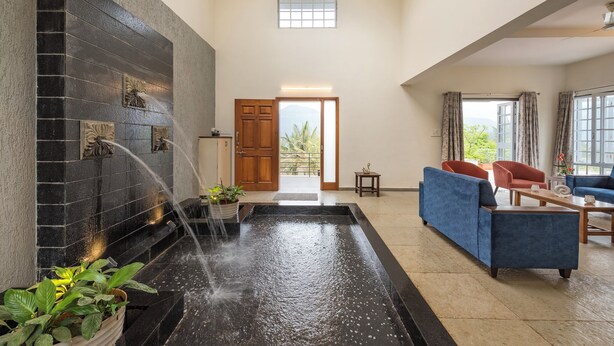 A spacious indoor area with a water feature, seating, and a view through a door. - CosmicStays GreyStone Villa Mountain View & Dam (Paud)
