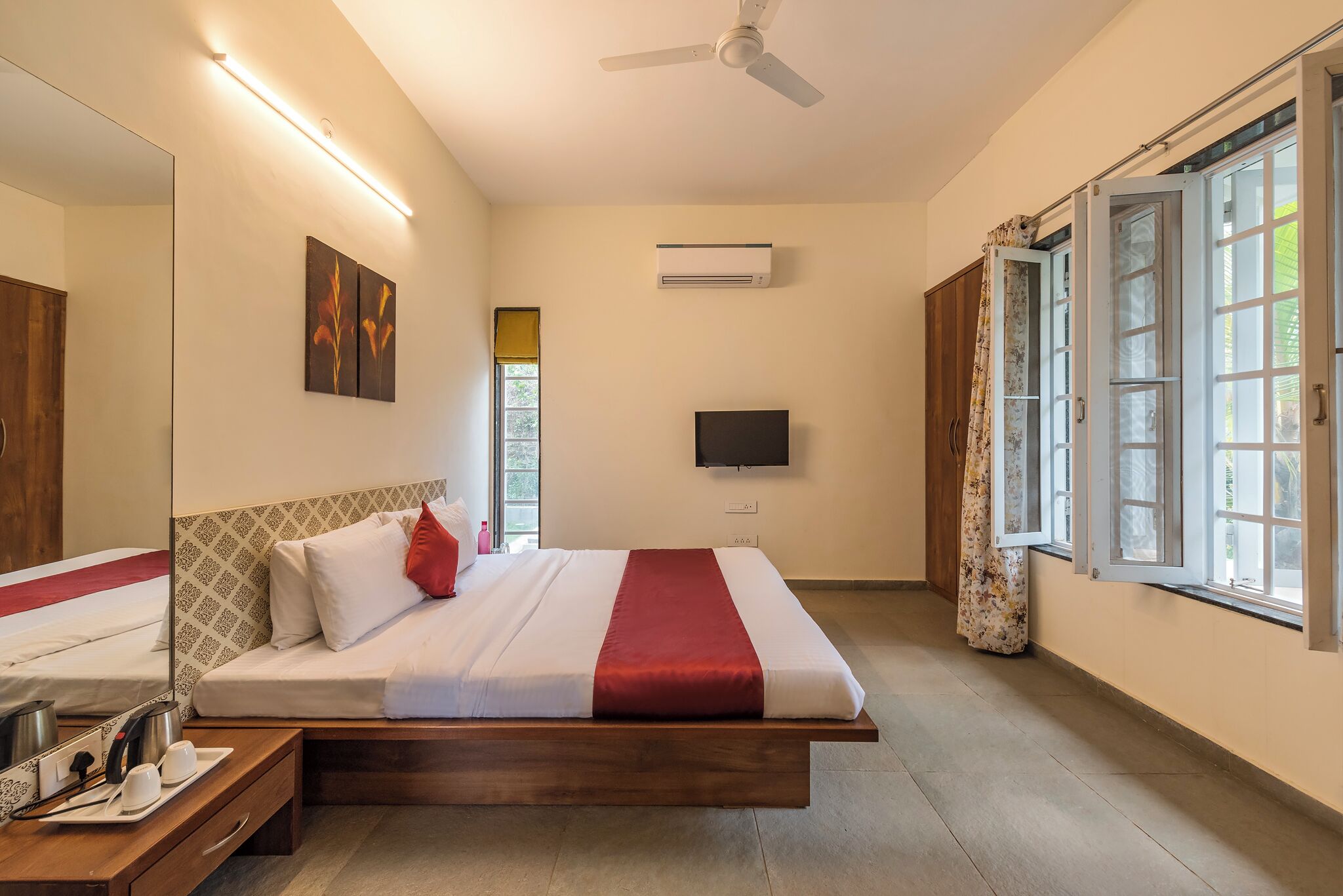A modern hotel room with a large bed, a flat-screen TV, an air conditioning unit, and a window with curtains.
