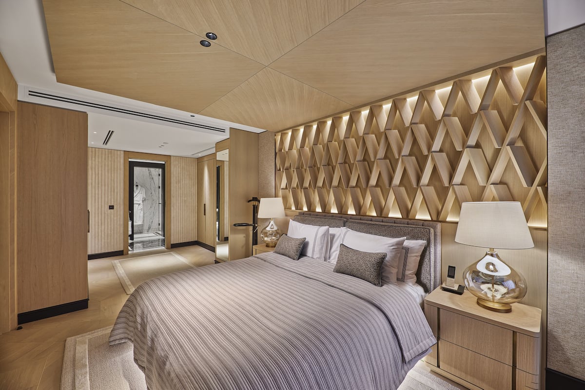 A modern bedroom with a large bed, a nightstand with lamps, and a geometric patterned wall.