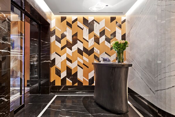 A modern lobby with a geometric patterned wall, a marble floor, and a large planter with flowers. - Vakko Hotel and Residence (Istanbul)