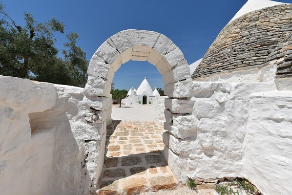 Un chemin en pierre en forme d’arche mène à un bâtiment blanc surmonté d’un toit en pierre.