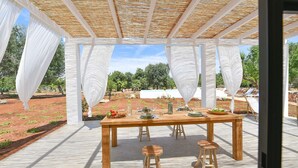 Un área de comedor al aire libre con una mesa y taburetes de madera, rodeada de cortinas blancas y un techo de madera.