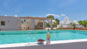Una piscina con agua cristalina, una botella de vino y un bol de cerezas.
