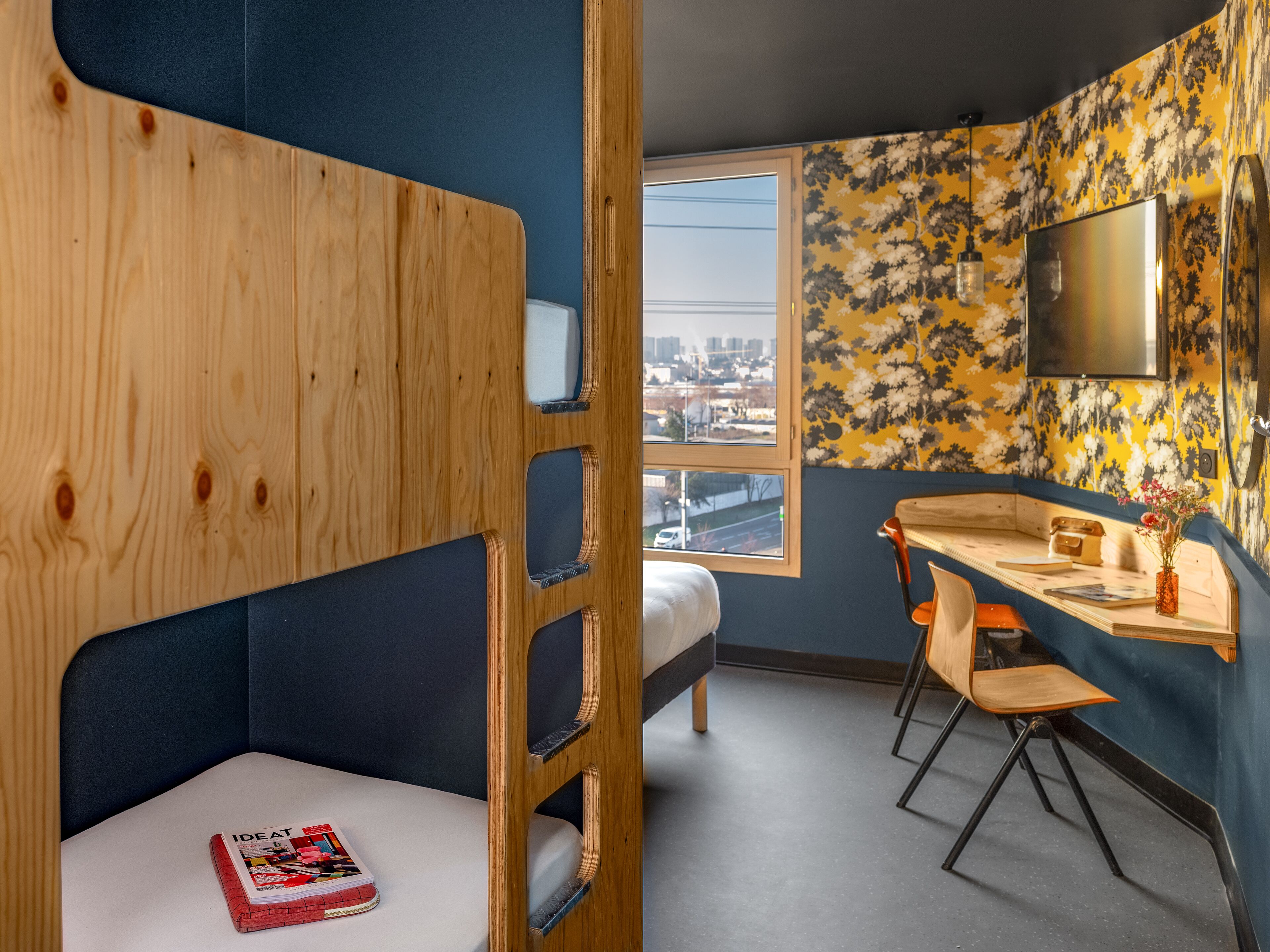 Una habitación con literas, un escritorio, una silla y una ventana con vista a la ciudad.