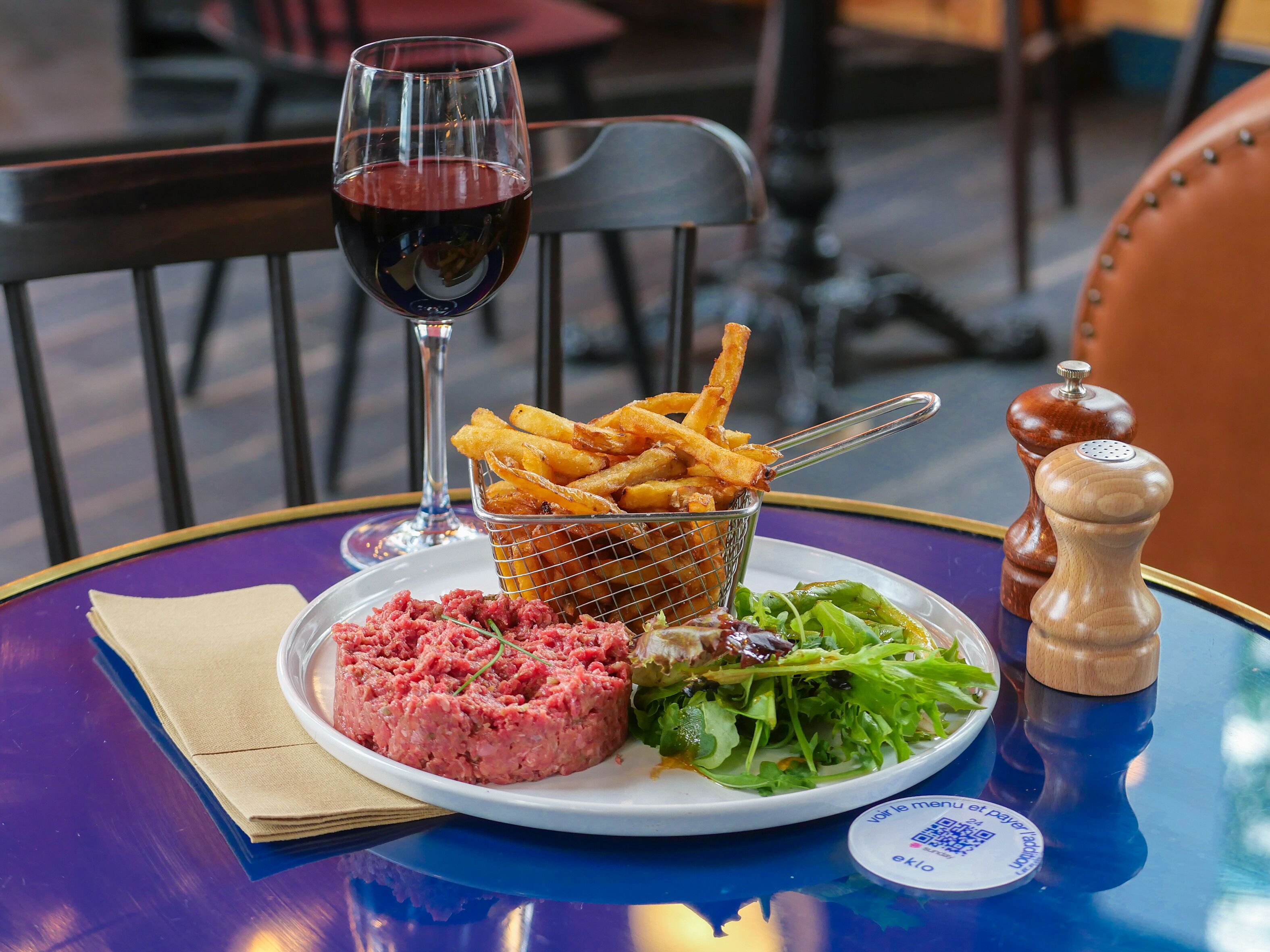 Ein Esstisch mit einer Speisenplatte, einem Glas Rotwein und einer Korb mit Pommes.