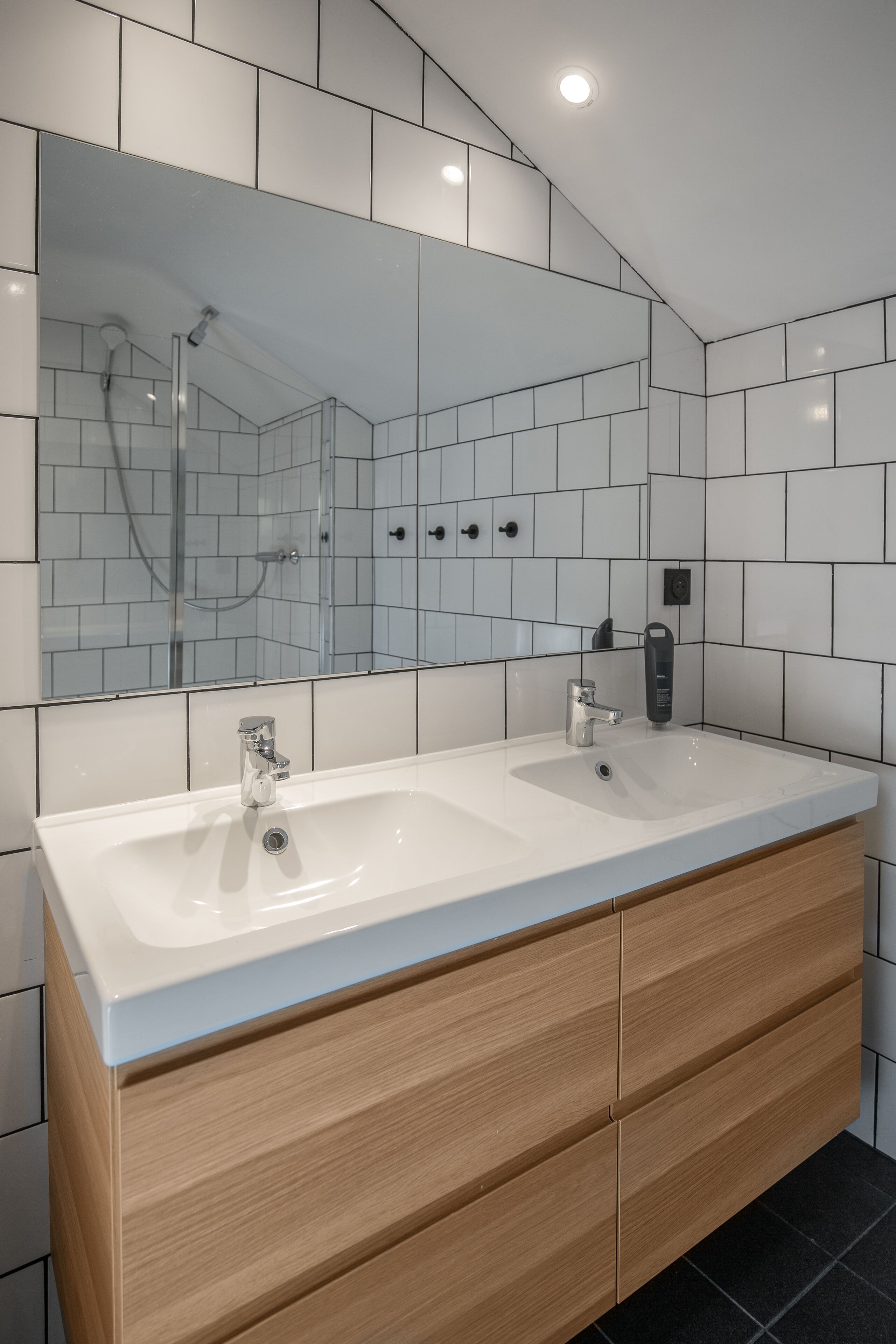 Ein modernes Badezimmer mit einem Doppelwaschbecken, Holzschränken und einem großen Spiegel.
