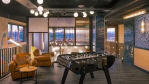 Un espacio interior moderno con mesa de fútbol, sofás de cuero, zona de bar y ventanas amplias que ofrecen vistas a la ciudad.