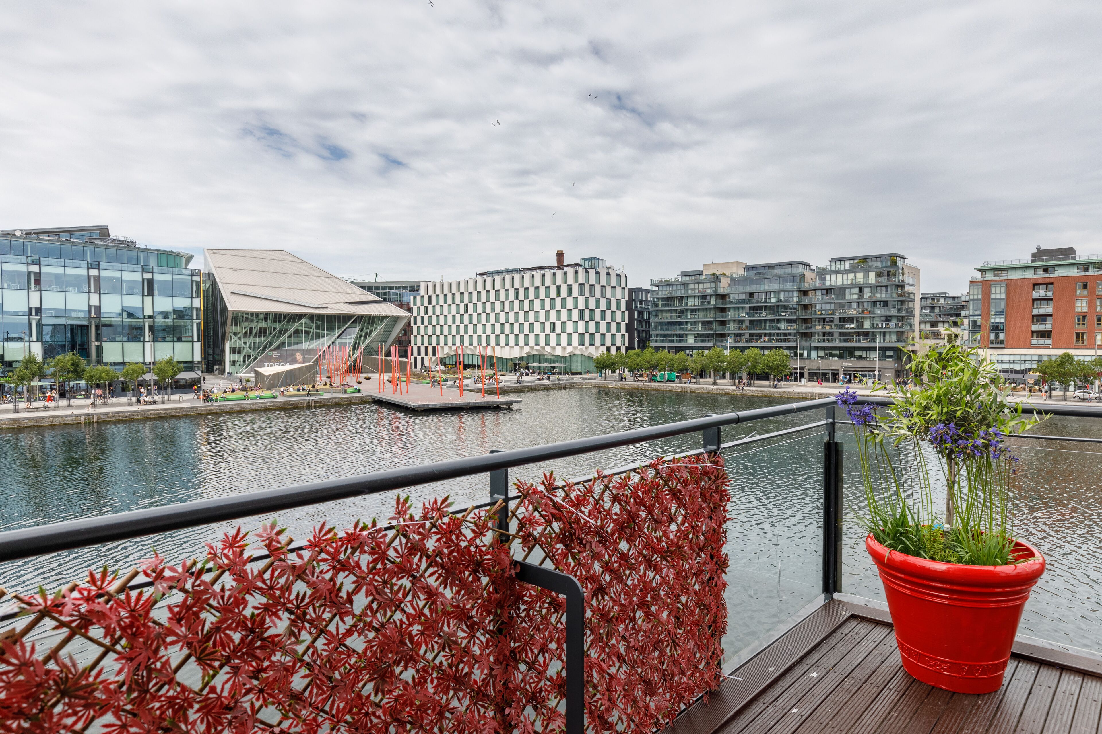 Un bâtiment moderne doté d’une façade en verre et d’un motif à carreaux, situé de l’autre côté d’une étendue d’eau.
