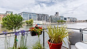Un balcon agrémenté de plantes en pot, offrant une vue sur une rivière et des bâtiments modernes.
