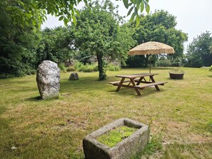 Ein Picknickbereich mit einem Holztisch, einer Bank, einem Reetdachschirm und Steinbauten.