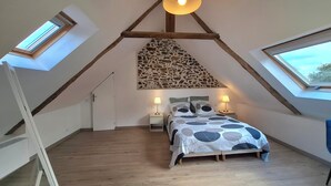 Une chambre avec un plafond en pente, des fenêtres de toit, un lit recouvert d’une couvre-lit à motifs, deux lampes de chevet et un mur d’accent en pierre.