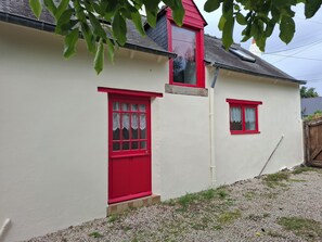 Ein weißes Gebäude mit roten Türen und Fenstern, einer kleinen Veranda und einem Schotterweg.