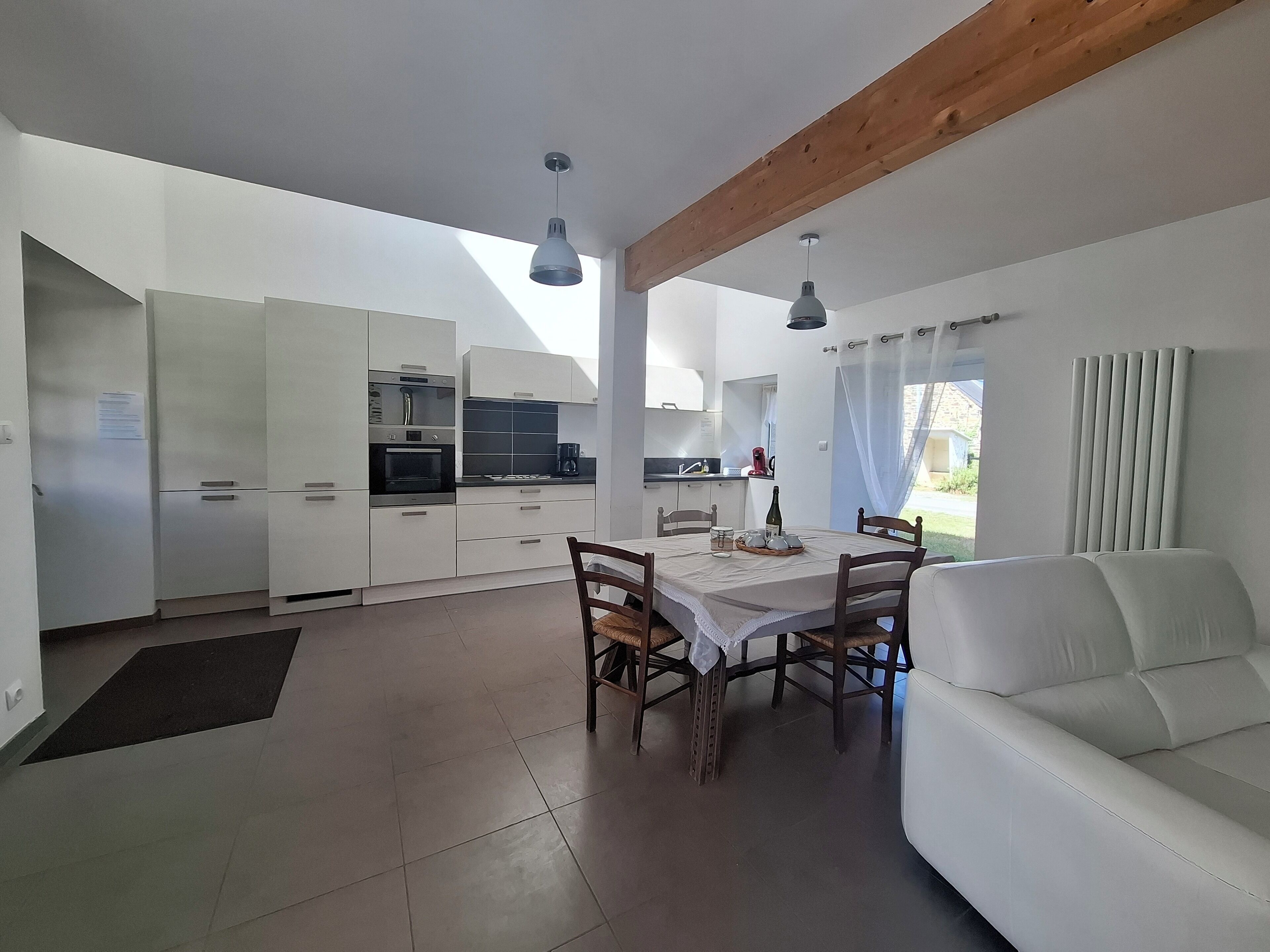 Cozinha moderna com armários brancos, uma mesa de jantar com cadeiras e um sofá branco.