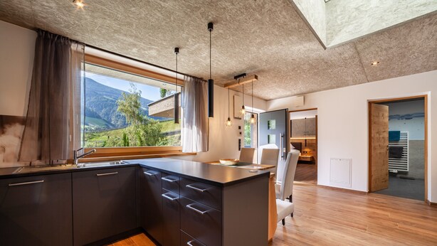 Eine moderne Küche mit einer großen Kochinsel, Holzboden und Blick auf eine gebirgige Landschaft.