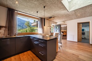 A modern kitchen with a large island, wooden flooring, and a view of a mountainous landscape. - Holiday Apartment 'Chalet Riad 2' with Mountain View and Outdoor Whirlpool (St. Martin / Saltaus)