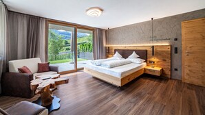 Ein modernes Schlafzimmer mit einem großen Bett, einer Couch, einem Holztisch und Blick auf Grünflächen.