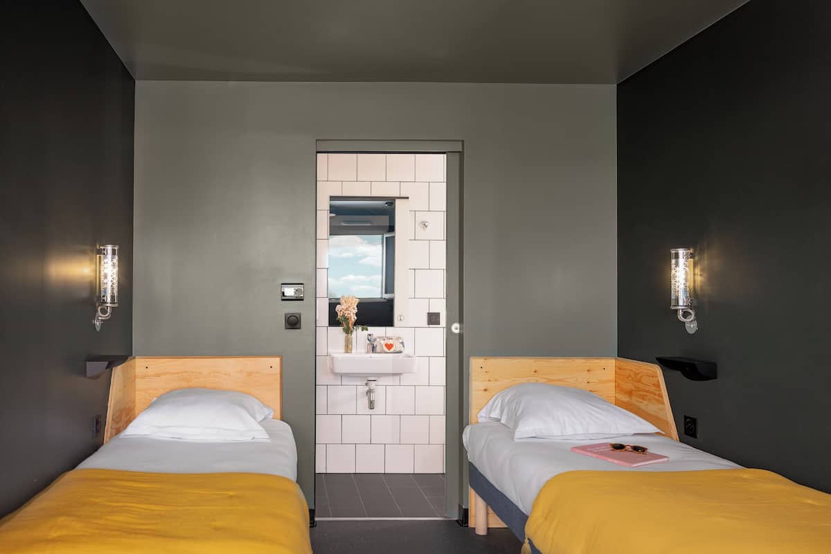 Habitación de hotel con dos camas individuales, un baño peque ño con espejo y dos lámparas de pared.