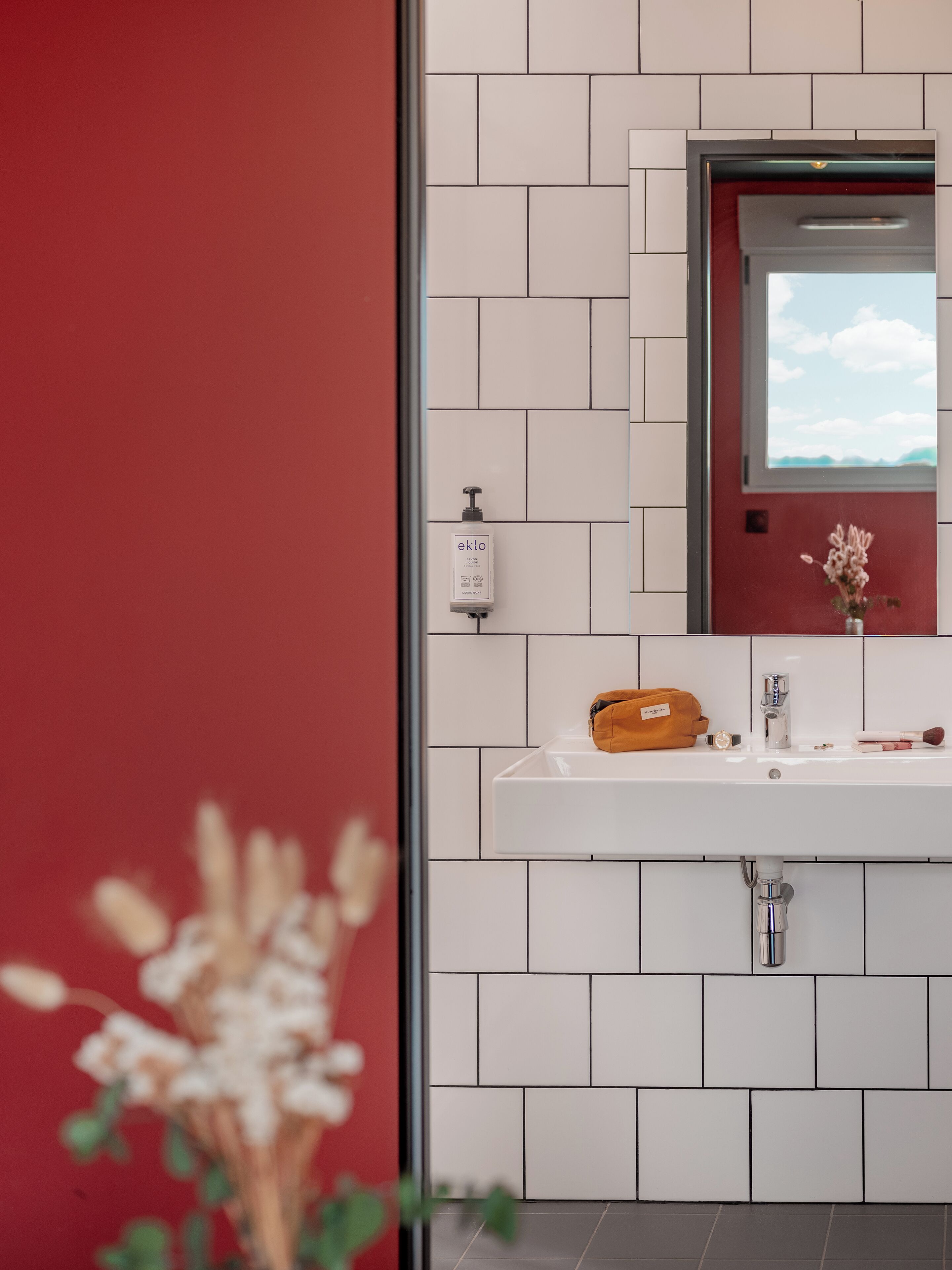 A bathroom with a white sink, a mirror, and a red wall.