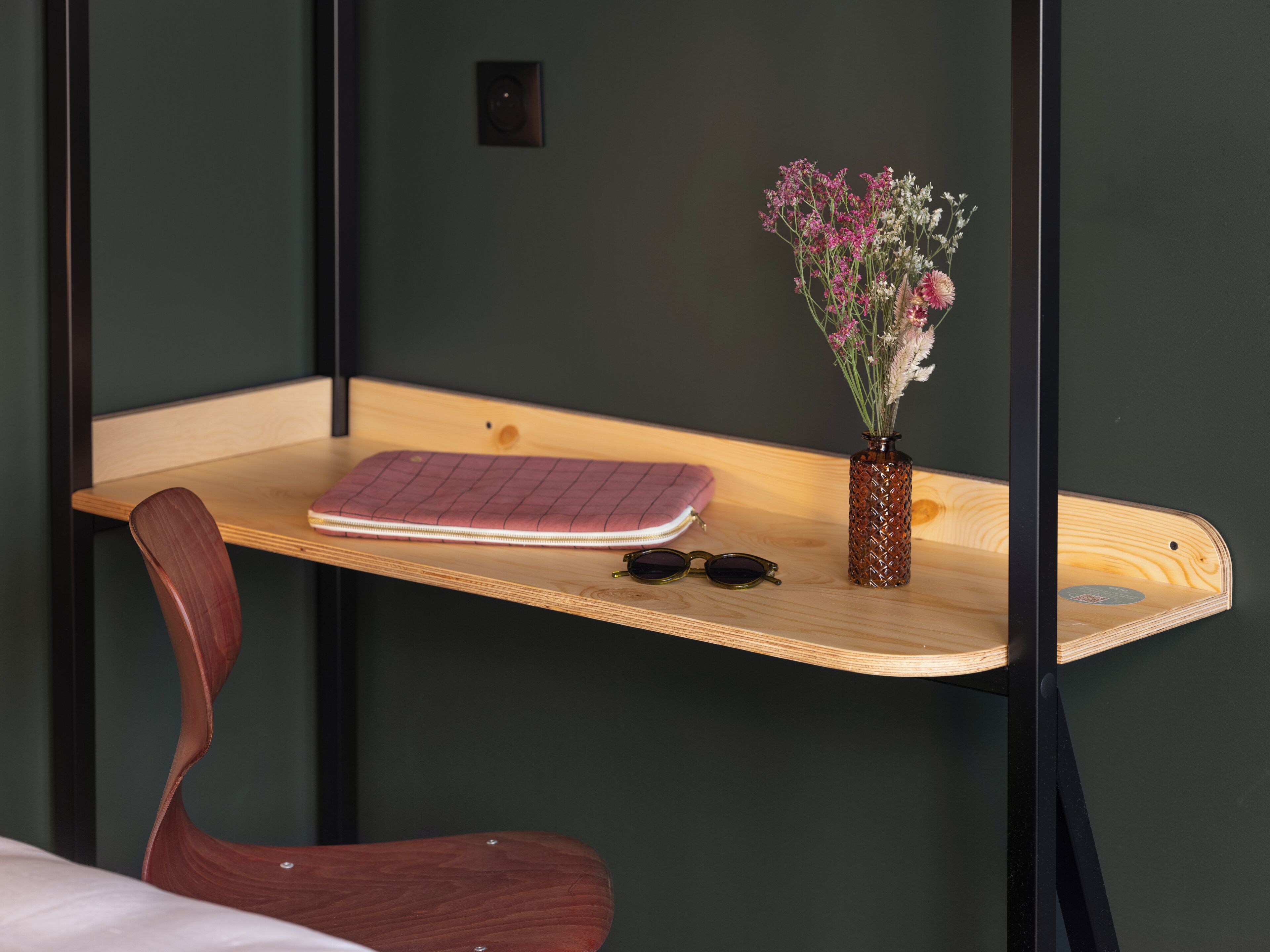 A wooden desk with a notebook, sunglasses, and a vase of flowers.