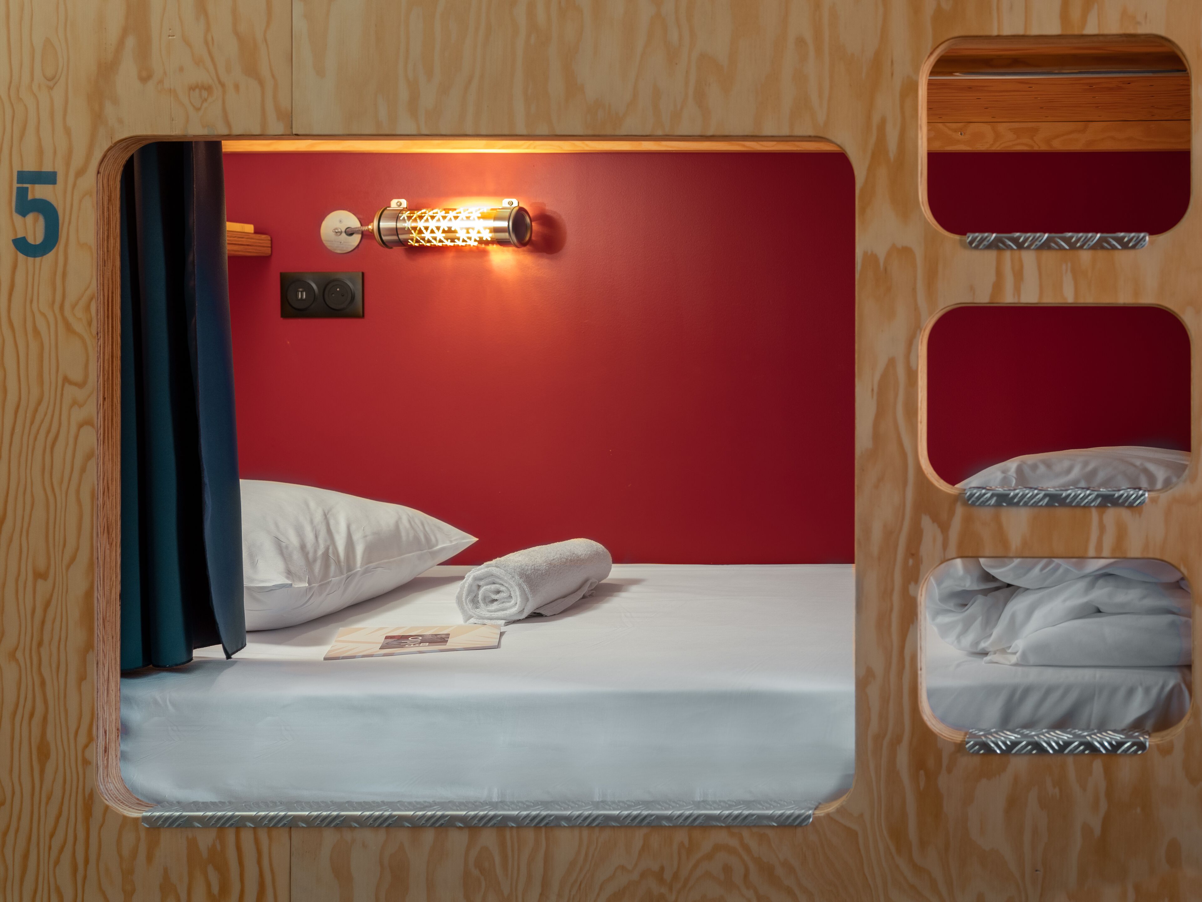 A compact room with a single bed, a wall-mounted light, and a small mirror.