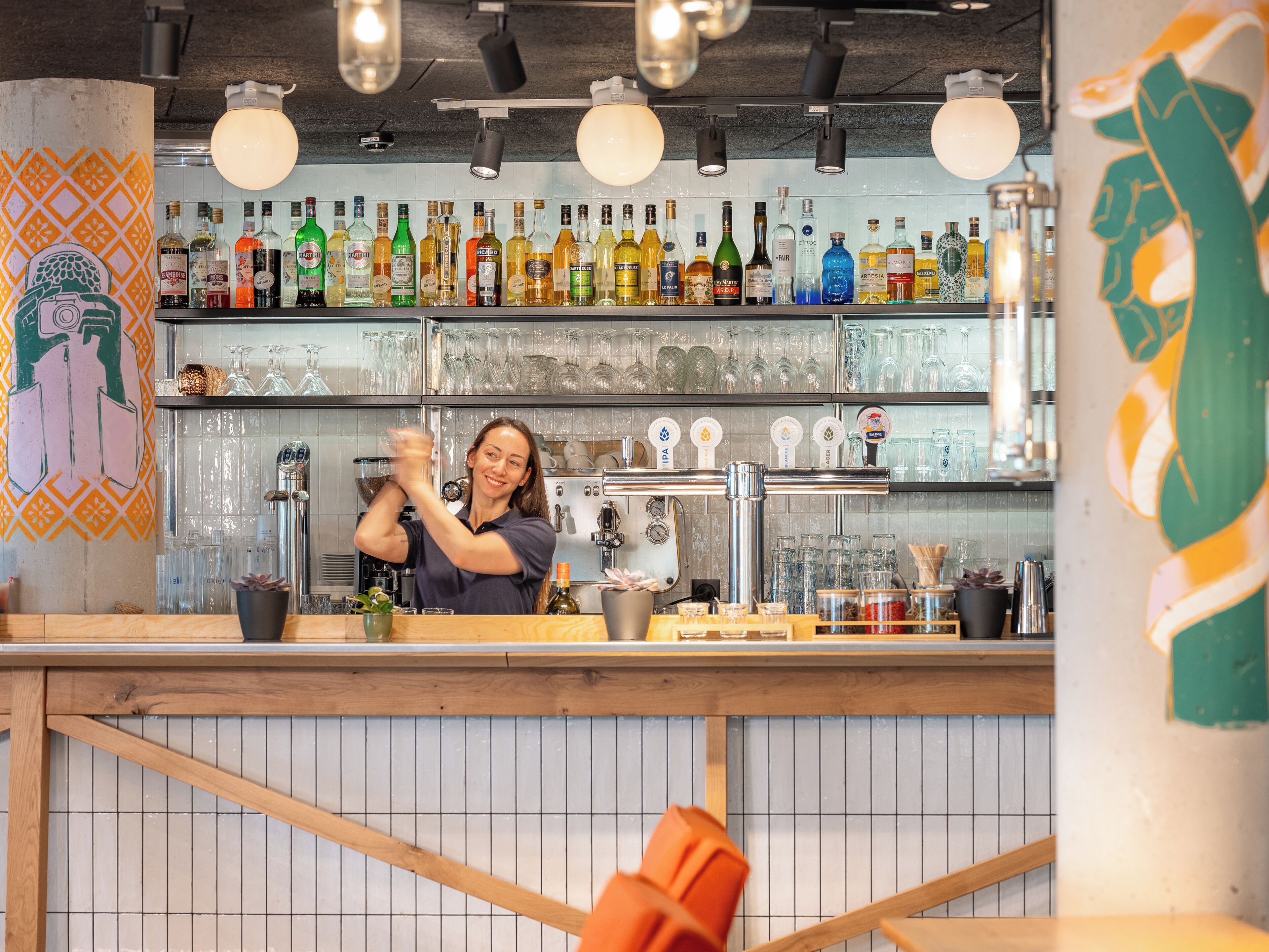 Zona de bar con estantes llenos de botellas de licores, un bartender y una barra con utensilios.