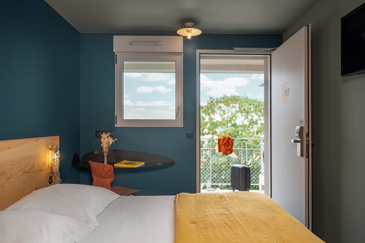 Un dormitorio con cama, mesita de noche, ventana con vistas y puerta que da a un balcón.