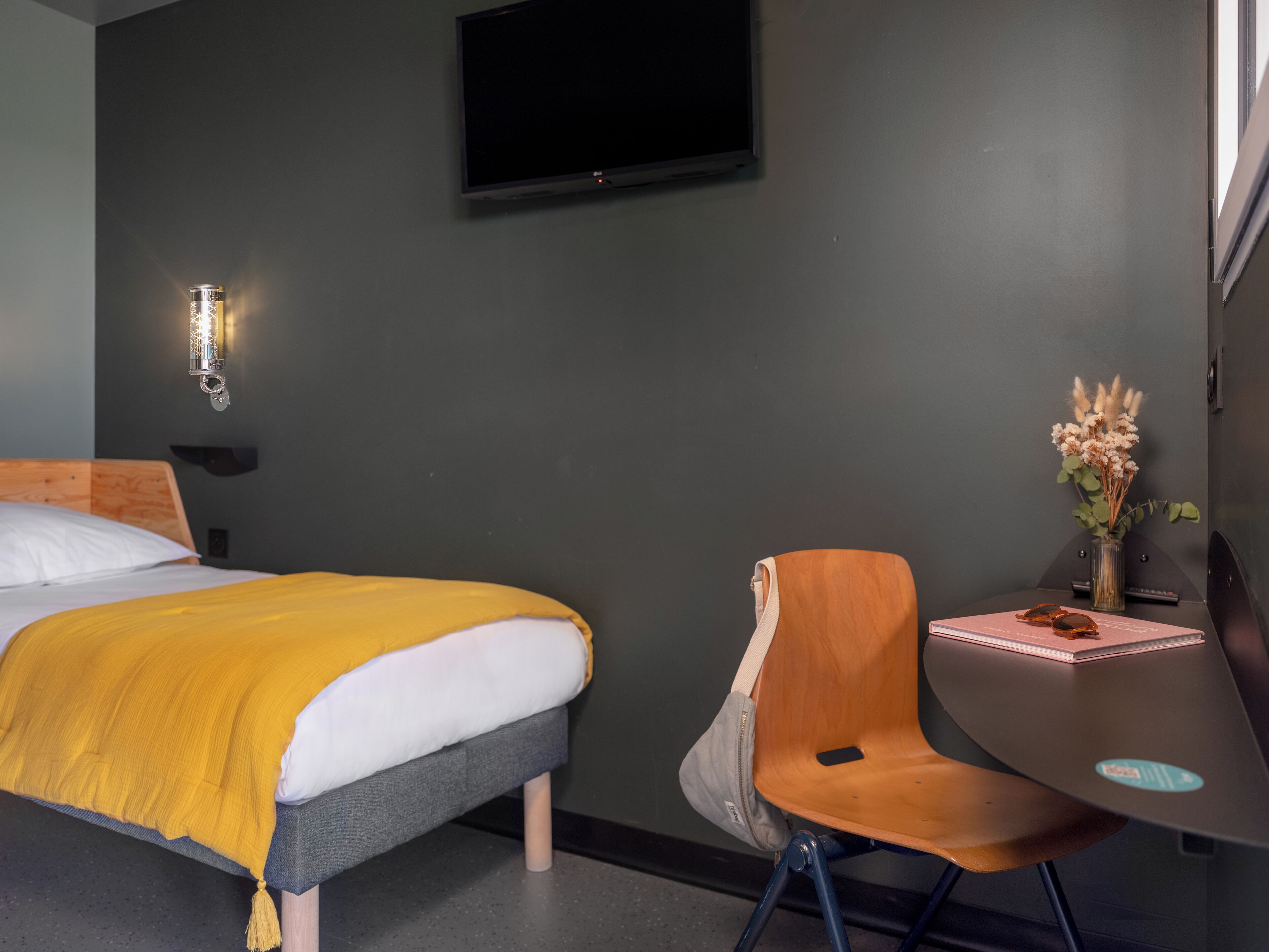 A hotel room with a bed, a desk, a chair, a TV, and a vase with flowers.