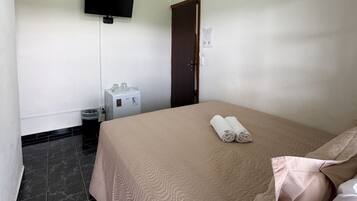 A hotel room with a bed, a ceiling fan, a television, a small refrigerator, and a door.