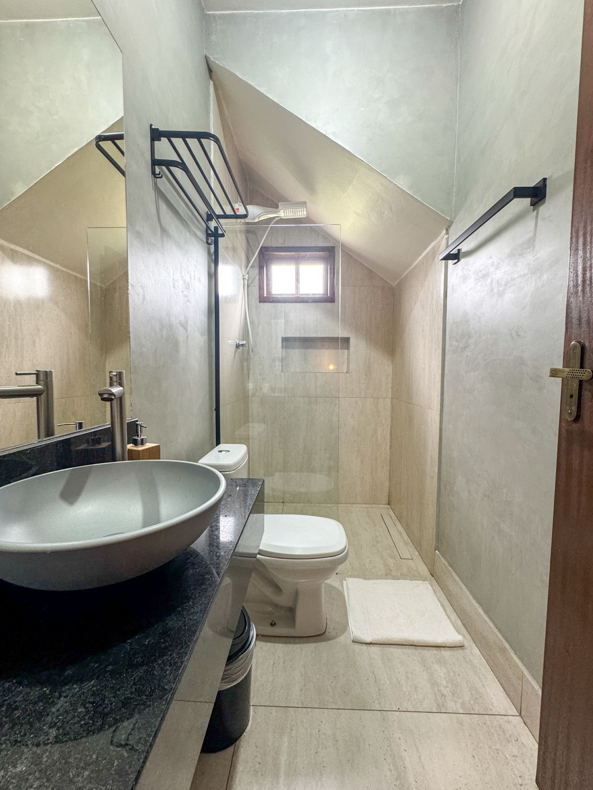 A modern bathroom with a large vessel sink, a toilet, a shower, and a small window.