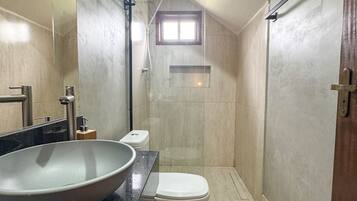 A modern bathroom with a large vessel sink, a toilet, a shower, and a small window.