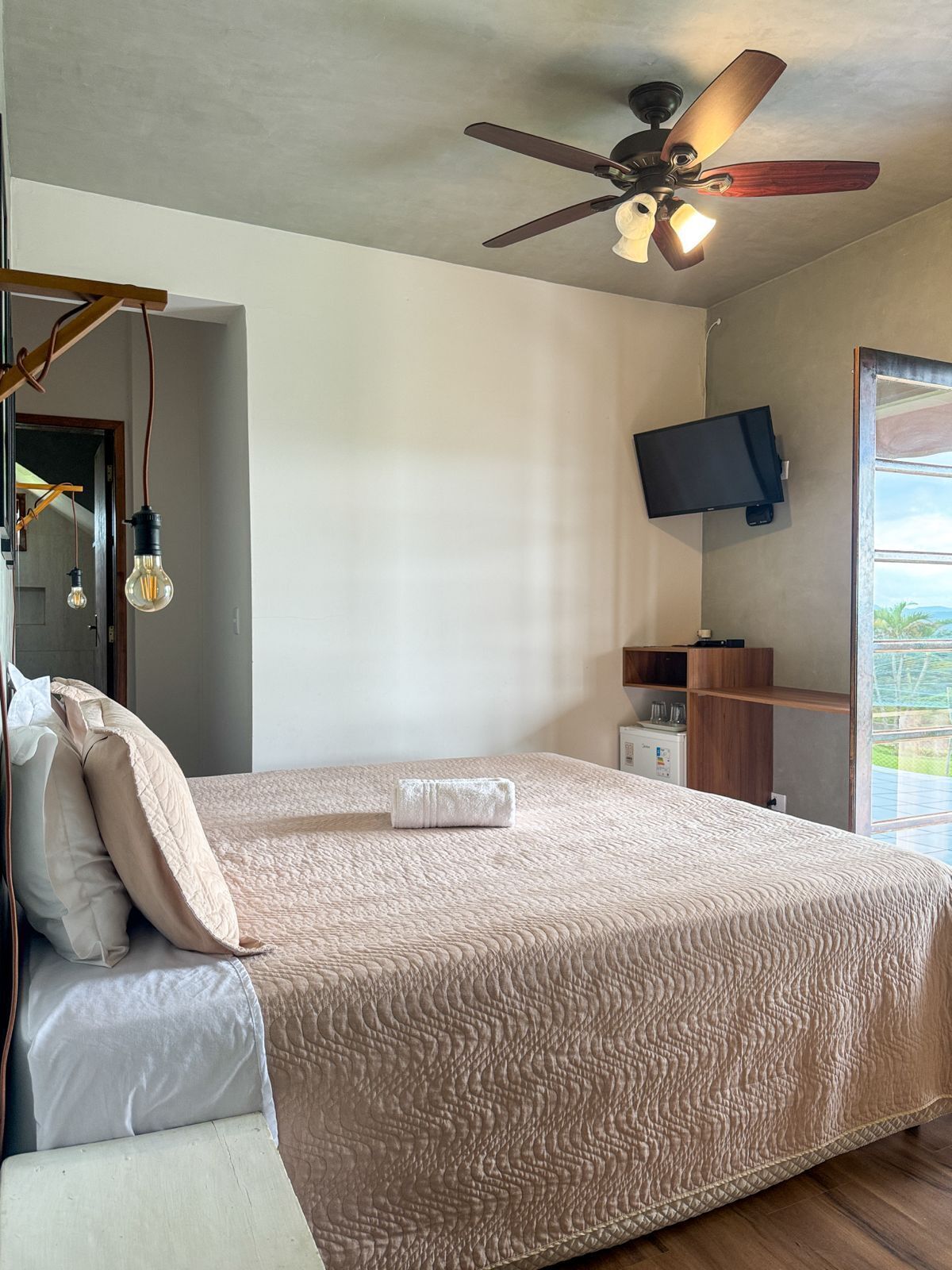 A bedroom with a bed, a ceiling fan, a TV, and a window.