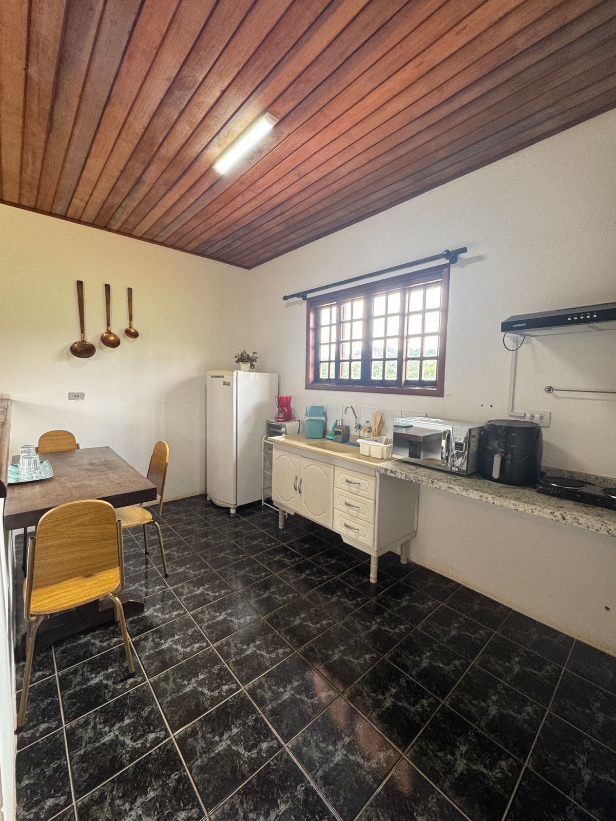 Uma cozinha com teto de madeira, janela, geladeira, pia e mesa de jantar com cadeiras.