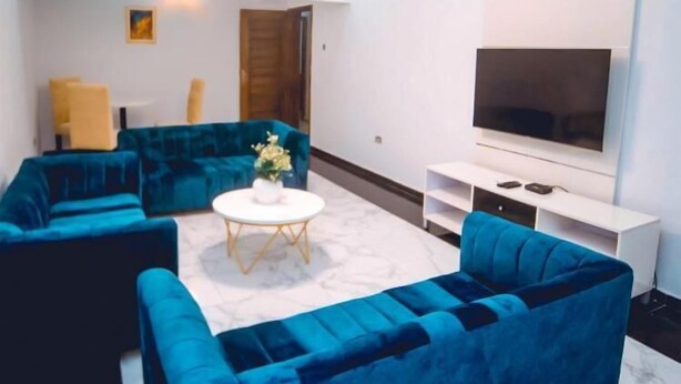 Una sala de estar moderna con un sofá azul, una mesa de centro blanca y un televisor de pantalla plana sobre un mueble blanco.