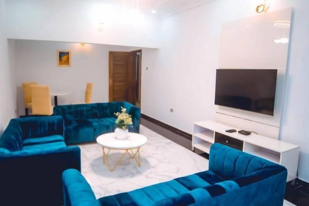A modern living room with a blue sofa set, a white coffee table, and a flat-screen TV on a white stand.
