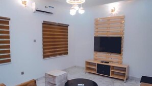 Una sala moderna con un conjunto de sofá, una mesa de centro, un televisor sobre un mueble de madera y una lámpara de techo.