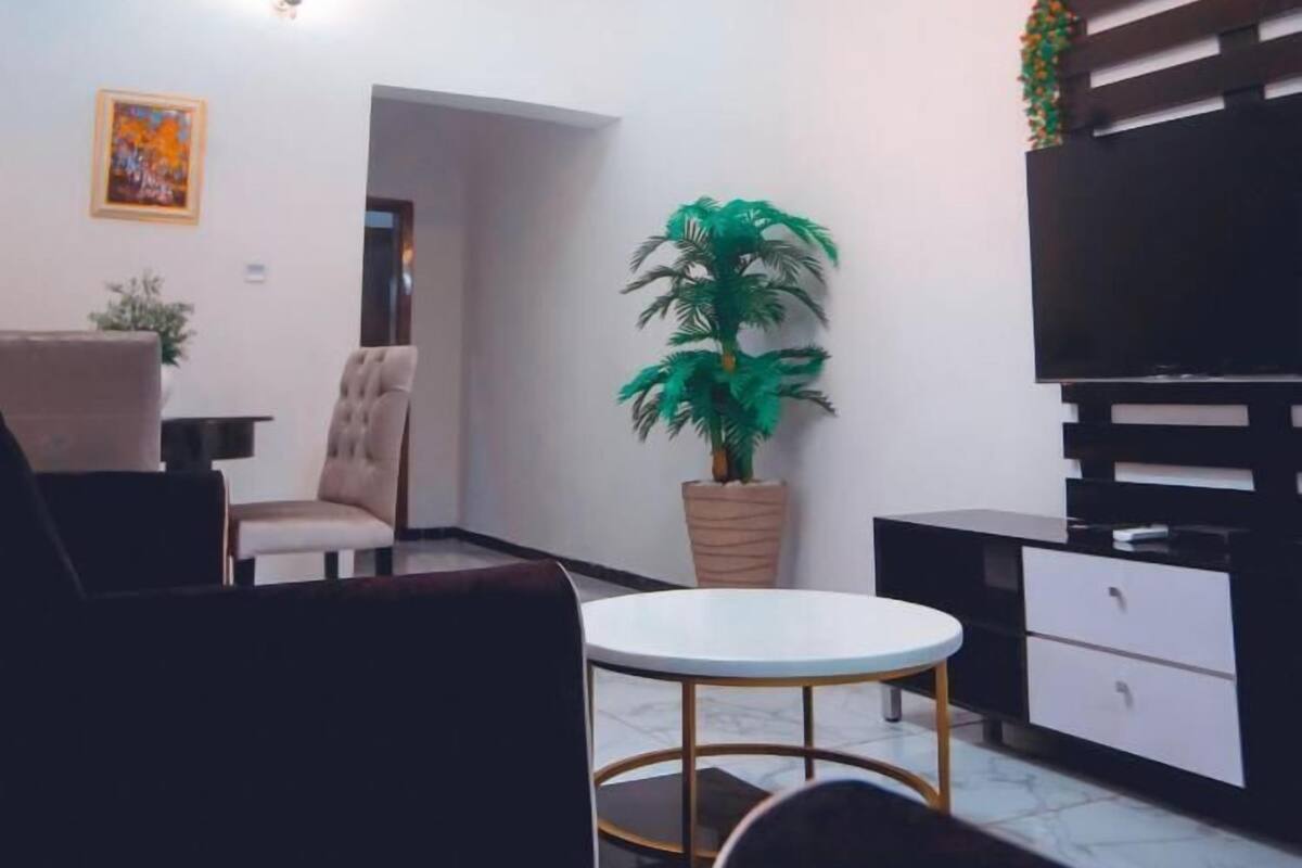 A modern living room with a round table, a sofa, a chair, a potted plant, and a built-in TV unit.