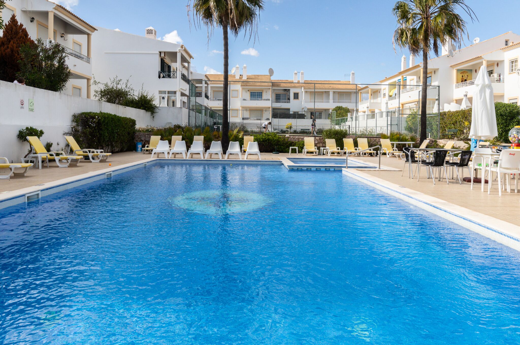 Ein Swimmingpool mit Liegestühlen und Sonnenschirmen, umgeben von weißen Gebäuden mit Balkonen.