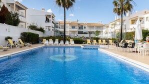 Une piscine entourée de bâtiments blancs dotés de balcons, avec des chaises longues et des parasols à proximité.